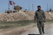 FILE - In this April 4, 2018 file photo, a U.S-backed Syrian Manbij Military Council soldier passes a U.S. position near the tense front line with Turkish-backed fighters, in Manbij, north Syria. President Donald Trump's abrupt decision to pull U.S. forces out of northeast Syria stunned the Kurds, who for the past three years have been America's partner in fighting the Islamic State group. The U.S. needed a partner on the ground after its takeover of the eastern and northern third of Syria, and found in the Kurds an effective, organized force. The U.S. armed the Kurdish militia, along with some Syrian Arabs and Christian Assyrians, and backed them with U.S. troops and airpower. (AP Photo/Hussein Malla, File)