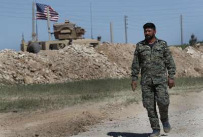 FILE - In this April 4, 2018 file photo, a U.S-backed Syrian Manbij Military Council soldier passes a U.S. position near the tense front line with Turkish-backed fighters, in Manbij, north Syria. President Donald Trump's abrupt decision to pull U.S. forces out of northeast Syria stunned the Kurds, who for the past three years have been America's partner in fighting the Islamic State group. The U.S. needed a partner on the ground after its takeover of the eastern and northern third of Syria, and found in the Kurds an effective, organized force. The U.S. armed the Kurdish militia, along with some Syrian Arabs and Christian Assyrians, and backed them with U.S. troops and airpower. (AP Photo/Hussein Malla, File)