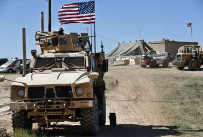 FILE - In this Wednesday, April 4, 2018 file photo, a U.S. soldier, left, sits on an armored vehicle behind a sand barrier at a newly installed position near the front line between the U.S-backed Syrian Manbij Military Council and the Turkish-backed fighters, in Manbij, north Syria. The U.S. military said Friday it has started pulling equipment, but not troops, out of Syria as a first step in meeting President Donald Trump's demand for a complete military withdrawal. (AP Photo/Hussein Malla, File)