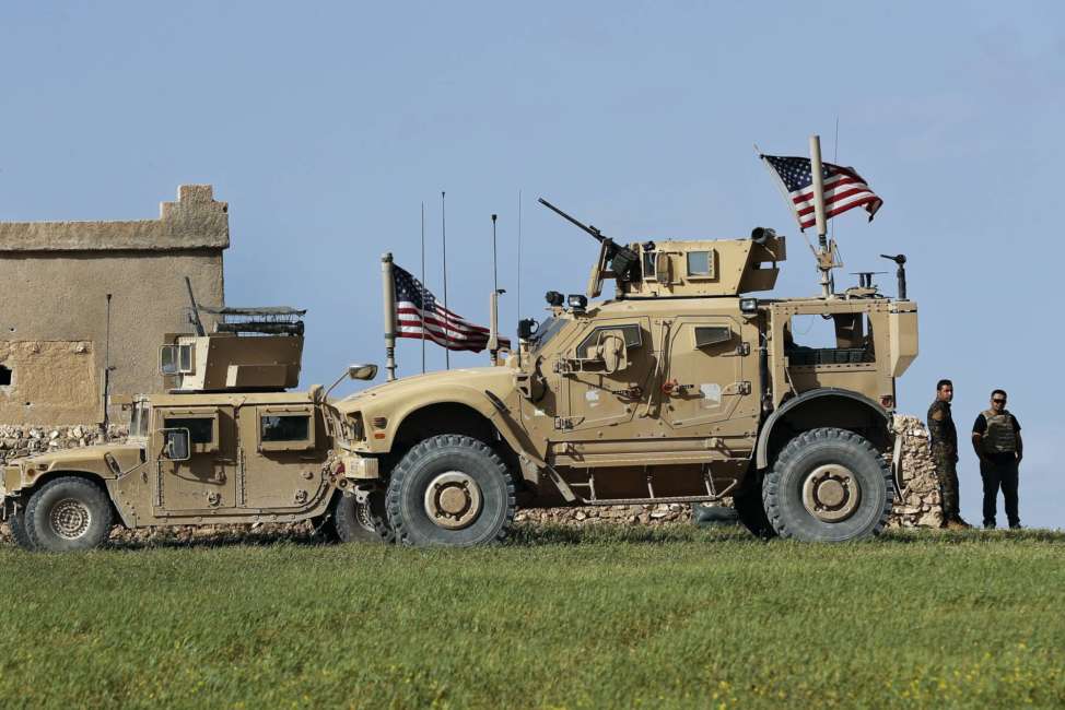 FILE - In this file picture taken on Thursday, March 29, 2018, a fighter, second from right, of U.S-backed Syrian Manbij Military Council stands next to U.S. humvee at a U.S. troop's outpost on a road leading to the tense front line between Syrian Manbij Military Council fighters and Turkish-backed fighters, at Halawanji village, north of Manbij, Syria.    A spokesman for the U.S.-led coalition said Friday, Jan. 11, 2019 that the process of withdrawal in Syria has begun, declining to comment on specific timetables or movements. (AP Photo/Hussein Malla, File)