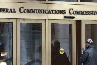 FILE - In this Thursday, Dec. 14, 2017, file photo, a person with a smartphone enters the Federal Communications Commission building in Washington. Tech companies and nearly two dozen U.S. states clashed with the government in federal court Friday, Feb. 1, 2019, over the repeal of net neutrality, a set of Obama-era rules aimed at preventing big internet providers from discriminating against certain technology and services. The action rolling back the neutrality rules 