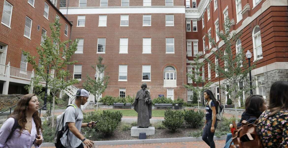 FILE - In this Sept. 1, 2016 file photo, students walk past a Jesuit statue in front of Isaac Hawkins Hall, center, formerly named Mulledy Hall, on the Georgetown University campus, in Washington. Georgetown University undergraduates have voted Thursday, April 11, 2019, in favor of a referendum seeking the establishment of a fund benefiting the descendants of enslaved people sold to pay off the school's debts. (AP Photo/Jacquelyn Martin, File)
