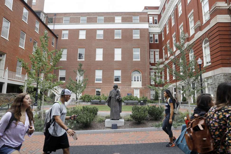 FILE - In this Sept. 1, 2016 file photo, students walk past a Jesuit statue in front of Isaac Hawkins Hall, center, formerly named Mulledy Hall, on the Georgetown University campus, in Washington. Georgetown University undergraduates have voted Thursday, April 11, 2019, in favor of a referendum seeking the establishment of a fund benefiting the descendants of enslaved people sold to pay off the school's debts. (AP Photo/Jacquelyn Martin, File)