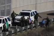 FILE - In this Dec. 9, 2018 file photo, a woman and children are ushered into cars by U.S. Border Patrol agents after crossing illegally over the border wall into San Diego, Calif., as seen from Tijuana, Mexico. A federal judge in California on Friday, May 17, 2019, will consider a challenge to President Donald Trump's plan to tap billions of dollars from the Defense and Treasury departments to build his prized border wall with Mexico. (AP Photo/Rebecca Blackwell, File)