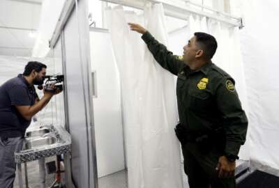 Border Patrol agent E. Flores shows the shower section during a media tour of a new U.S. Customs and Border Protection temporary facility near the Donna International Bridge, Thursday, May 2, 2019, in Donna, Texas. Officials say the site will primarily be used as a temporary site for processing and care of unaccompanied migrant children and families and will increase the Border Patrol's capacity to process migrant families. (AP Photo/Eric Gay)