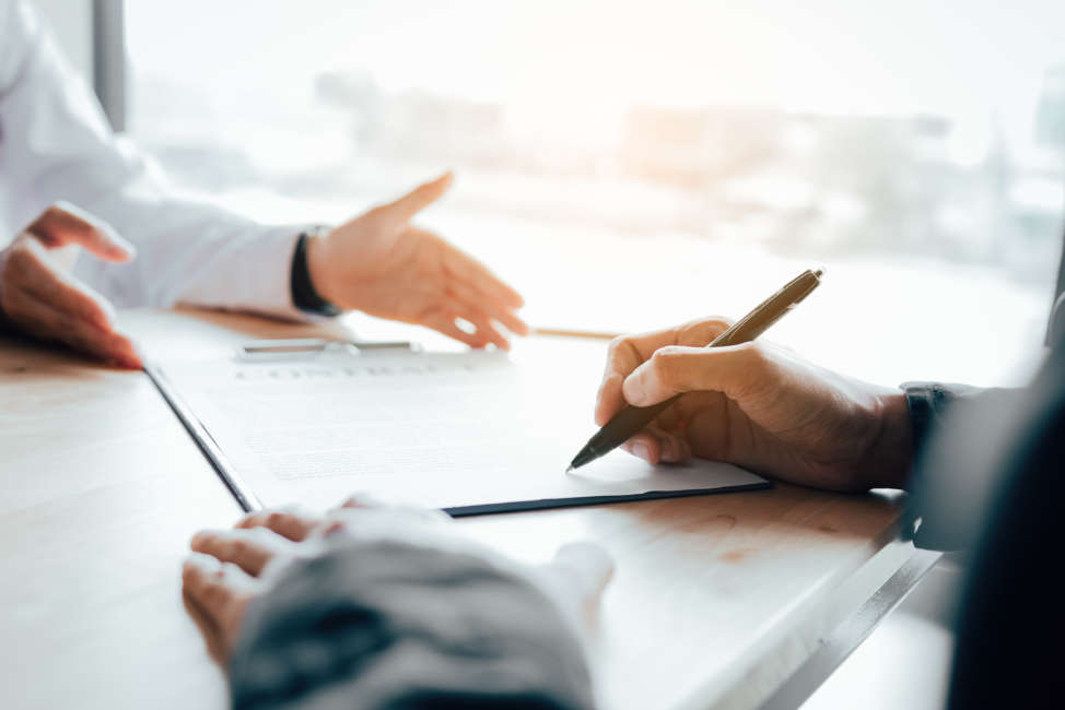 Client signing a real estate contract on desk in office.