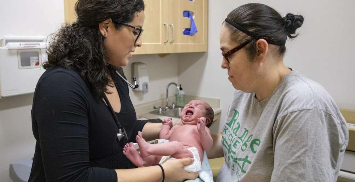 In this Aug. 13, 2019, photo, Dr. Jasmine Saavedra, left, a pediatrician at Esperanza Health Centers in Chicago, hands newborn Alondra Marquez to her mother, Esthela Nuñez, right, after examination. Doctors and public health experts warn of poor health outcomes and rising costs they say will come from sweeping changes that would deny green cards to many immigrants who use Medicaid, as well as food stamps and other forms of public assistance. (AP Photo/Amr Alfiky)