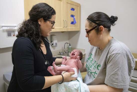 In this Aug. 13, 2019, photo, Dr. Jasmine Saavedra, left, a pediatrician at Esperanza Health Centers in Chicago, hands newborn Alondra Marquez to her mother, Esthela Nuñez, right, after examination. Doctors and public health experts warn of poor health outcomes and rising costs they say will come from sweeping changes that would deny green cards to many immigrants who use Medicaid, as well as food stamps and other forms of public assistance. (AP Photo/Amr Alfiky)
