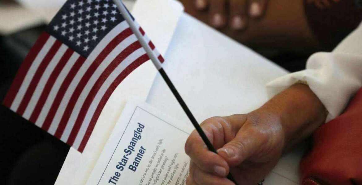 FILE - In this Aug. 16, 2019, file photo a citizen candidate holds an American flag and the words to The Star-Spangled Banner before the start of a naturalization ceremony at the U.S. Citizenship and Immigration Services Miami field office in Miami. U.S. Citizenship and Immigration Services officers can now create fictitious social media accounts to monitor information on foreigners seeking visas, green cards and citizenship.(AP Photo/Wilfredo Lee)