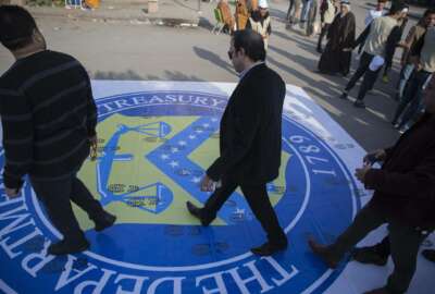 Iraqi protesters walk over a big poster with the logo of the US Department Of The Treasury, that was spread on the street by the organizers to show disrespect, during a rally for the Shiite group Asaib Ahl al-Haq, in Baghdad, Iraq, Saturday, Dec. 14, 2019.   (AP Photo/Nasser Nasser)