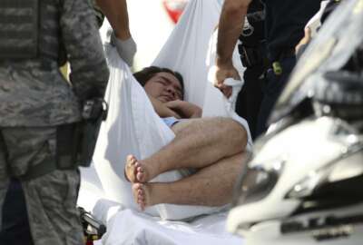 An unidentified male is taken away on a stretcher outside the main gate at Joint Base Pearl Harbor-Hickam, Wednesday, Dec. 4, 2019, in Hawaii, following a shooting. (AP Photo/Caleb Jones)
