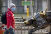 A man wearing a face mask walks past statues of bulls in Beijing, Friday, Feb. 28, 2020. Asian stock markets fell further Friday on spreading virus fears, deepening an global rout after Wall Street endured its biggest one-day drop in nine years. (AP Photo/Mark Schiefelbein)