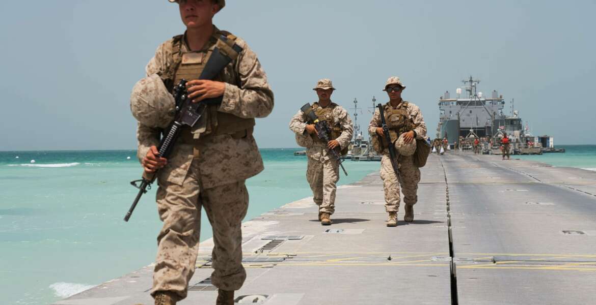 U.S. Marines walk down a removable Trident Pier leading to an American ship docked near an Emirati military base home to a Military Operations and Urban Terrain facility in al-Hamra, United Arab Emirates, Monday, March 23, 2020. U.S. Marines and Emirati forces held the biennial exercise, called Native Fury, that saw forces seize a sprawling model Mideast city. The drill on Monday was conducted amid tensions with Iran and despite the global new coronavirus pandemic. (AP Photo/Jon Gambrell)