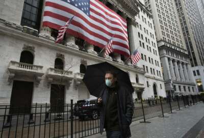 A man wearing a mask walks by the New York Stock Exchange, Tuesday, March 17, 2020. Share prices are volatile after a brutal sell-off that gave the U.S. stock market its worst loss in more than three decades. Markets in Europe lost early gains and were trading lower on Tuesday (AP Photo/Mark Lennihan)