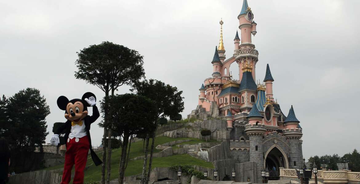FILE - In this June 8, 2018 file photo, Mickey Mouse poses in front of the castle of Sleeping Beauty at Disneyland Paris, in Chessy, France, east of Paris. Theme parks at Walt Disney World Resort in Florida and Disneyland Paris Resort will be closing through the end of the month, starting at the close of business Sunday, the Walt Disney Company announced. For most people, the new coronavirus causes only mild or moderate symptoms. For some it can cause more severe illness. (AP Photo/Francois Mori, File)