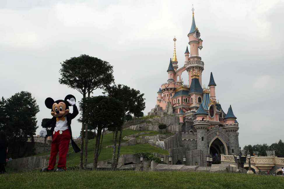 FILE - In this June 8, 2018 file photo, Mickey Mouse poses in front of the castle of Sleeping Beauty at Disneyland Paris, in Chessy, France, east of Paris. Theme parks at Walt Disney World Resort in Florida and Disneyland Paris Resort will be closing through the end of the month, starting at the close of business Sunday, the Walt Disney Company announced. For most people, the new coronavirus causes only mild or moderate symptoms. For some it can cause more severe illness. (AP Photo/Francois Mori, File)