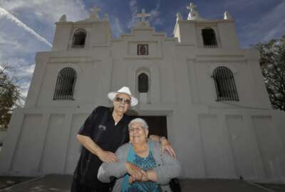 Frank and Ester Cota pose for a photograph outside Our Lady of Guadalupe church Friday, Jan. 24, 2020 in Guadalupe, Ariz. Founded by Yaqui Indian refugees from Mexico more than a century ago, Guadalupe is named for Mexico's patron saint, Our Lady of Guadalupe, and is fiercely proud of its history. The town known for sacred Easter rituals featuring deer-antlered dancers also is wary of outsiders as it prepares for the 2020 census. (AP Photo/Matt York)