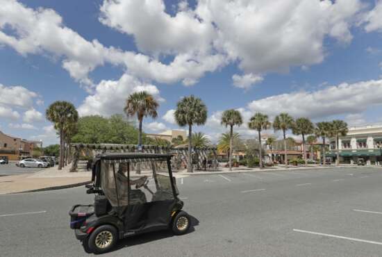In this Thursday, March 19, 2020 photo, a resident drives his golf cart down what usually is a busy street by the Spanish Springs town square in The Villages, Fla. Three town squares in the community are closed due to the coronavirus through the end of the month in what is perhaps the largest concentration of seniors in the U.S. (AP Photo/John Raoux)