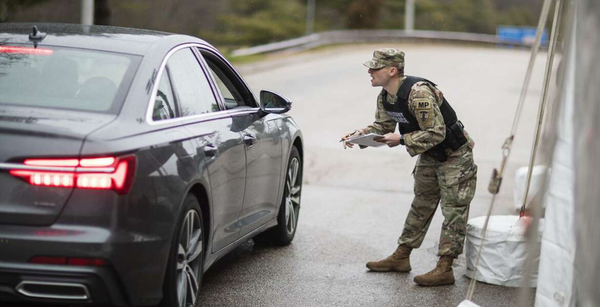 A member of the Rhode Island National Guard Military Police talks with a motorist with New York license plates at a checkpoint on I-95 near the border with Connecticut where New Yorkers must pull over and provide contact information and are told to self-quarantine for two weeks, Saturday, March 28, 2020, in Hope Valley, R.I. Rhode Island Gov. Gina Raimondo on Saturday ordered anyone visiting the state to self-quarantine for 14 days and restricted residents to stay at home and nonessential retail businesses to close Monday until April 13 to help stop the spread of the coronavirus. (AP Photo/David Goldman)