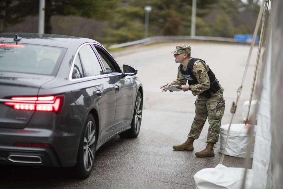 A member of the Rhode Island National Guard Military Police talks with a motorist with New York license plates at a checkpoint on I-95 near the border with Connecticut where New Yorkers must pull over and provide contact information and are told to self-quarantine for two weeks, Saturday, March 28, 2020, in Hope Valley, R.I. Rhode Island Gov. Gina Raimondo on Saturday ordered anyone visiting the state to self-quarantine for 14 days and restricted residents to stay at home and nonessential retail businesses to close Monday until April 13 to help stop the spread of the coronavirus. (AP Photo/David Goldman)