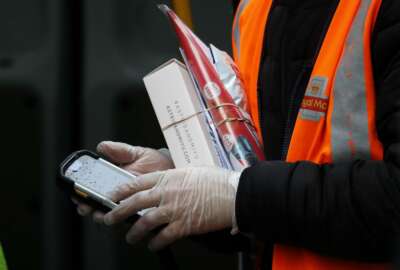 In this March 5, 2020, photo, a Royal Mail employee wears gloves as he hold parcels and the signature handheld as he delivers in London. While white collar workers trying to avoid contagion can work from home or call in sick if they experience symptoms of the new virus, such precautions are not an options for the millions of waiters, delivery workers, cashiers, ride-hailing drivers, museum attendants and countless others who routinely come into contact with the public. (AP Photo/Frank Augstein)