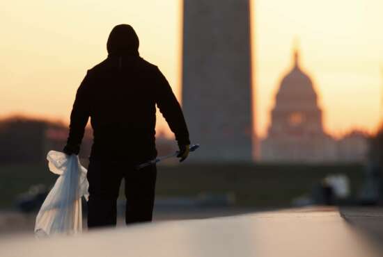 A National Park Service worker picks up trash along the drained Lincoln Memorial Reflecting Pool as the Washington Monument and the U.S. Capitol are seen in the distance in Washington, at sunrise Wednesday, March 18, 2020. The number of tourist is down ahead of an expected surge in coronavirus cases. (AP Photo/Carolyn Kaster)