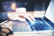 Side view of female hands using laptop with digital business interface on desk with blurry coffee cup and other items. Technology and finance concept. Double exposure