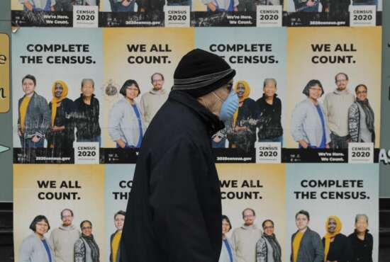 A man wearing a mask walks past posters encouraging participation in the 2020 Census, Wednesday, April 1, 2020, in Seattle's Capitol Hill neighborhood. Wednesday is Census Day, the date used to reference where a person lives for the once-a-decade count, as the U.S. is almost paralyzed by the spread of the novel coronavirus, but census officials vowed the job would be completed by its year-end deadline. (AP Photo/Ted S. Warren)