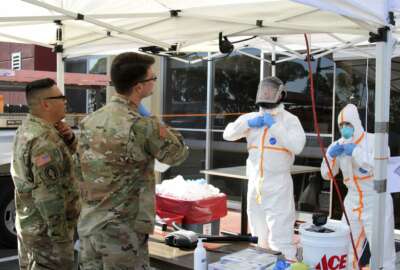 This March 27, 2020 photo provided by the California Army National Guard shows Sgt. Jose A. Magana, left, and Pfc. Michael Daggi of the California National Guard's Medical Detachment instructing California Emergency Medical Service Authority (EMSA) staff members on properly removing personal protective equipment at a San Mateo County COVID-19 treatment facility in Burlingame, Calif. Cal Guard's medical teams are actively assisting local and state agencies contain the coronavirus epidemic. This treatment facility houses patients who tested positive for COVID-19. (Staff Sgt. Eddie Siguenza/Army National Guard via AP))