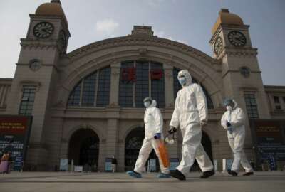 Workers in protective overalls walk past the Hankou railway station on the eve of its resuming outbound traffic in Wuhan in central China's Hubei province on Tuesday, April 7, 2020. Just after midnight Wednesday, the city's 11 million residents will be permitted to leave without special authorization as long as a mandatory smartphone application shows they are healthy and have not been in recent contact with anyone confirmed to have the virus. (AP Photo/Ng Han Guan)