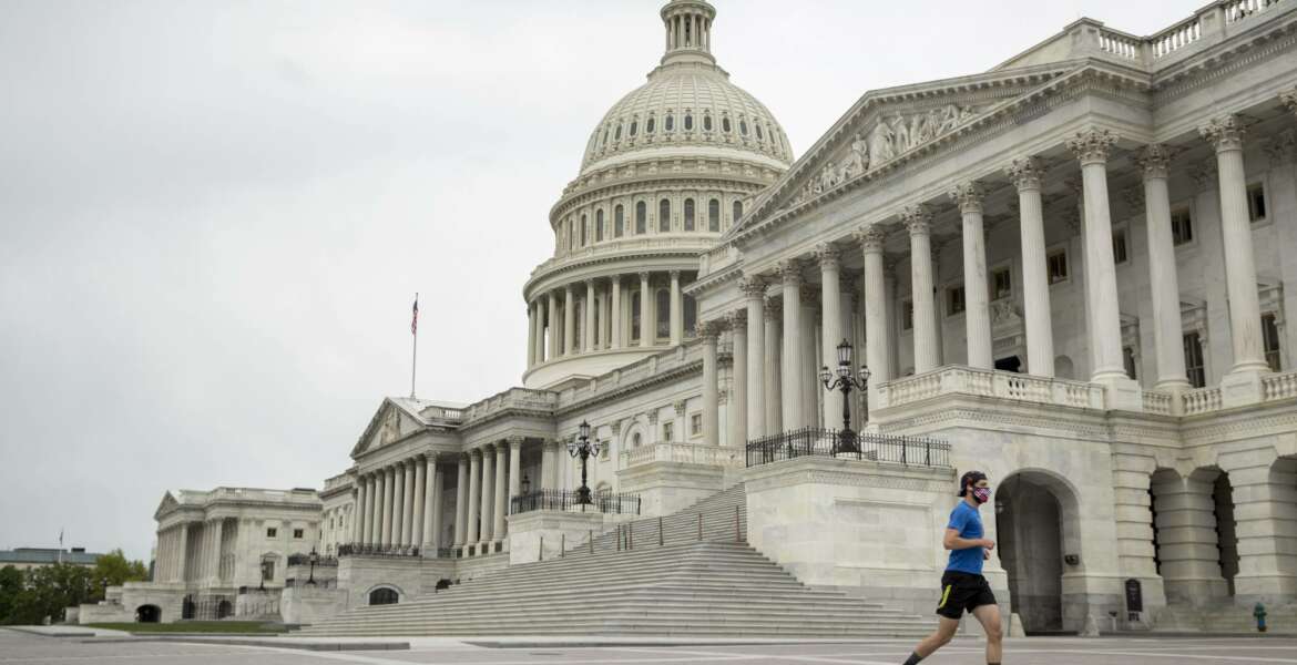 A man wearing a mask depicting American flags jogs past the U.S. Capitol Building, Tuesday, April 28, 2020, in Washington. The U.S. House of Representatives has canceled plans to return next week, a reversal after announcing it a day earlier. (AP Photo/Andrew Harnik)
