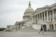 A man wearing a mask depicting American flags jogs past the U.S. Capitol Building, Tuesday, April 28, 2020, in Washington. The U.S. House of Representatives has canceled plans to return next week, a reversal after announcing it a day earlier. (AP Photo/Andrew Harnik)