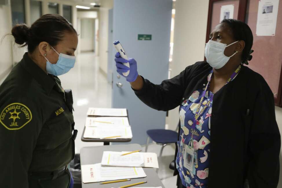 In this April 16, 2020, photo Sonia Munoz, left, custody assistant, gets her temperature taken at the hospital ward of the Twin Towers jail  in Los Angeles. Across the country first responders who've fallen ill from COVID-19, recovered have begun the harrowing experience of returning to jobs that put them back on the front lines of America's fight against the novel coronavirus. (AP Photo/Chris Carlson)