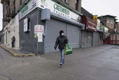 In this Friday, April 3, 2020, photo, a woman walks by local stores during the coronavirus pandemic in New York. Small business owners hoping for quick help from the government’s emergency $349 billion lending program were still waiting Tuesday, April 7, 2020, amid reports of computer problems at the Small Business Administration.(AP Photo/Mark Lennihan)