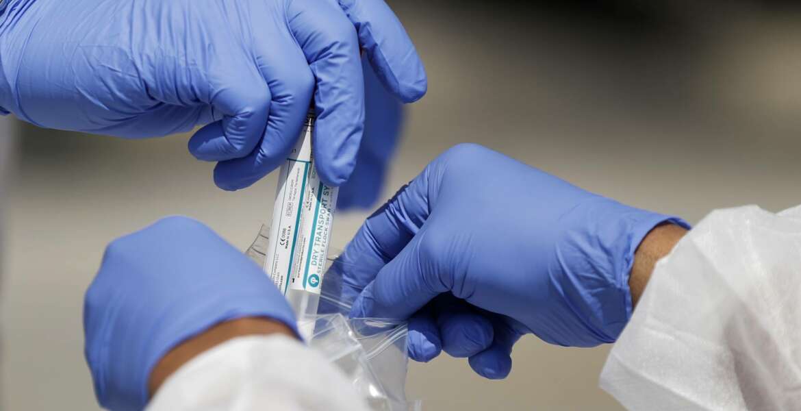 FILE - In this April 16, 2020, file photo, vials containing nasal swabs collected at a COVID-19 drive-through testing site are dropped into a plastic bag to be sent off for processing after being collected in St. Louis. An Associated Press review of more than 20 states found that before the coronavirus outbreak many had at least a modest supply of N95 masks, gowns, gloves and other medical equipment. But those supplies often were well past their expiration dates, left over from the H1N1 influenza outbreak a decade ago. (AP Photo/Jeff Roberson, File)