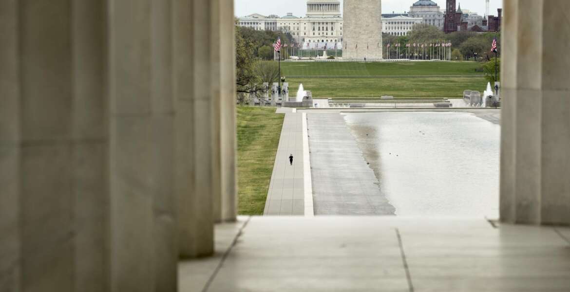 FILE - In this March 31, 2020, file photo the Dome of the U.S. Capitol and the Washington Monument are visible as a lone woman runs along the Reflecting Pool on the National Mall in Washington. The nation's capital, like most of the nation itself, is largely shuttered. (AP Photo/Andrew Harnik, File)