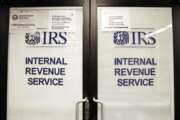 FILE - In this Jan. 16, 2019, file photo, doors at the Internal Revenue Service (IRS) in the Henry M. Jackson Federal Building are locked and covered with blinds as a sign posted advises that the office will be closed during the partial government shutdown in Seattle. (AP Photo/Elaine Thompson, File)