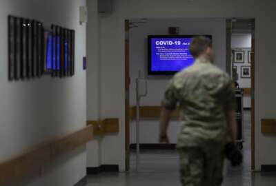 FILE - In this March 25, 2020, file photo a member of the U.S. Army walks down the hall toward a monitor displaying COVID-19 safety information in Fort Meade, Md. As of last week, the Army had already exceeded its retention goal of 50,000 soldiers for the fiscal year ending in September, re-enlisting more than 52,000 so far. (AP Photo/Carolyn Kaster, File)