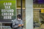 In this April 3, 2020, photo, a man wearing a face mask due to COVID-19 concerns stands outside a check cashing service center in the Brooklyn borough of New York. While millions of U.S. workers have already received a quick relief payment from the federal treasury through direct deposit, millions of others without traditional bank accounts must wait weeks for paper checks. Advocates for the poor say this is an opportunity to get many of those who are unbanked into the formal financial system. (AP Photo/Bebeto Matthews)