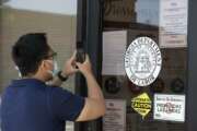 A man uses his phone to copy phone numbers posted on the locked doors of a Georgia Department of Labor office Thursday, May 7, 2020, in Norcross Ga. (AP Photo/John Bazemore)