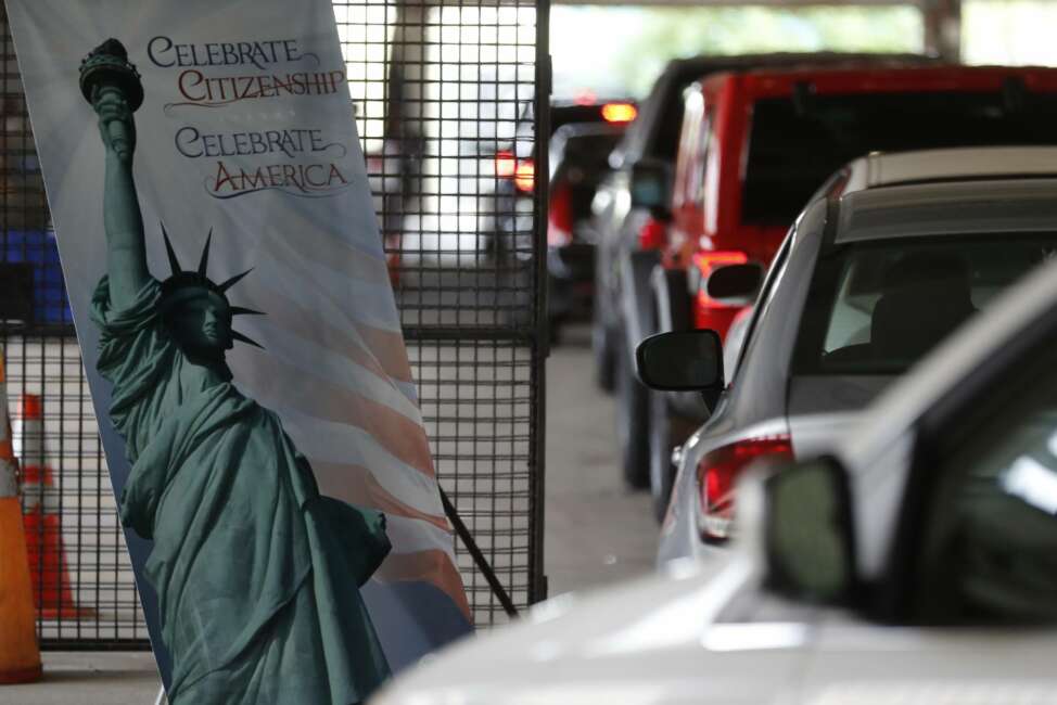 In this June 26, 2020, photo cars line up during a drive-thru naturalization service in a parking structure at the U.S. Citizenship and Immigration Services headquarters on Detroit's east side. The ceremony is a way to continue working as the federal courthouse is shut down due to Coronavirus. The U.S. has resumed swearing in new citizens but the oath ceremonies aren't the same because of COVID-19 and a budget crisis at the citizenship agency threatens to stall them again.  (AP Photo/Carlos Osorio)