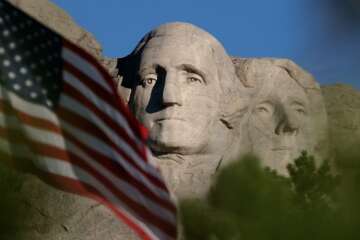 FILE - In this Sept. 11, 2002, file photo, the sun rises on Mt. Rushmore National Memorial near Keystone, S.D. as the flag is flown at half staff in honor of the first anniversary of the Sept. 11 terrorist attacks against the United States. President Donald Trump is planning to kick off Independence Day weekend in South Dakota with a show of patriotism _ fireworks popping, fighter jets thundering overhead and revelers crowding beneath a piece of classic Americana _ Mount Rushmore. (AP Photo/Laura Rauch, File)