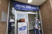 FILE - In this June 4, 2020, file photo, a customer walks out of a U.S. Post Office branch and under a banner advertising a job opening, in Seattle. The U.S. government will issue its latest snapshot Thursday, June 18, of the layoffs that have left millions unemployed but have slowed as businesses have increasingly reopened and rehired some of their laid-off workers. (AP Photo/Elaine Thompson, File)