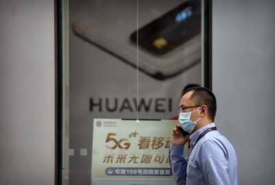 A man wearing a face mask to protect against the new coronavirus talks on his smartphone as he walks past a Huawei store in Beijing, Wednesday, July 1, 2020. China on Wednesday demanded Washington stop 