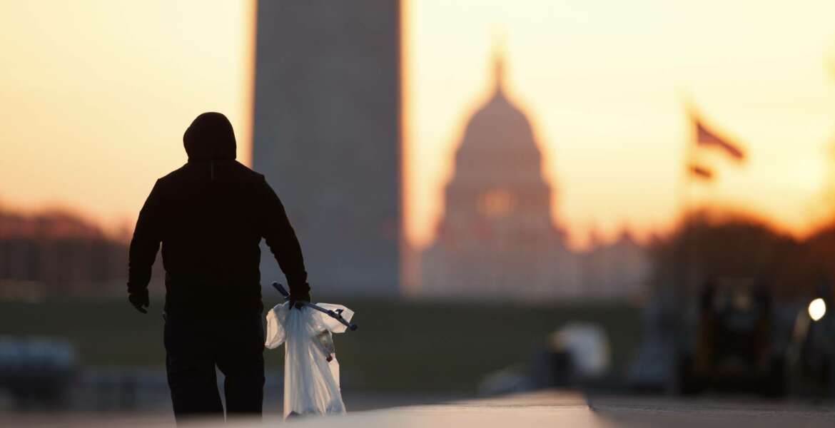 FILE - In this March 18, 2020, file photo a National Park Service worker picks up trash along the drained Lincoln Memorial Reflecting Pool as the Washington Monument and the U.S. Capitol are seen in the distance in Washington, at sunrise. Nearly 3,000 federal workers have filed compensation claims for having contracted COVID-19 on the job, a number that is expected to double by early next month, according to a Department of Labor review. (AP Photo/Carolyn Kaster, File)