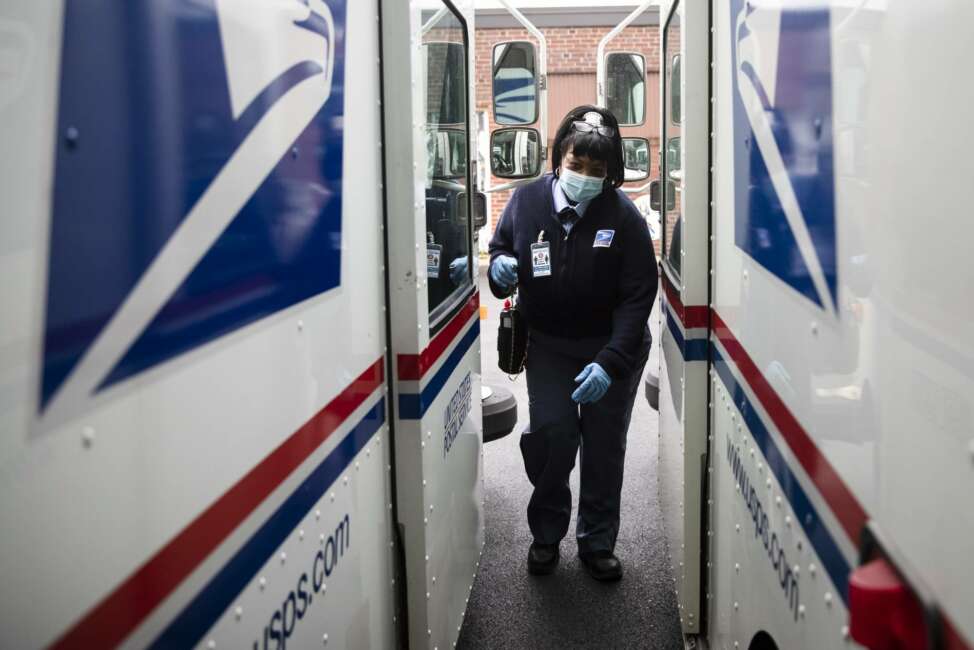 FILE - In this May 6, 2020, photo, United States Postal Service carrier Henrietta Dixon gets into her truck to deliver mail in Philadelphia.  Officials from six states and the District of Columbia are in court Thursday, Sept. 24,  to ask a federal judge to halt alleged slowdowns at the U.S. Postal Service that they say threaten the upcoming presidential election(AP Photo/Matt Rourke, File)