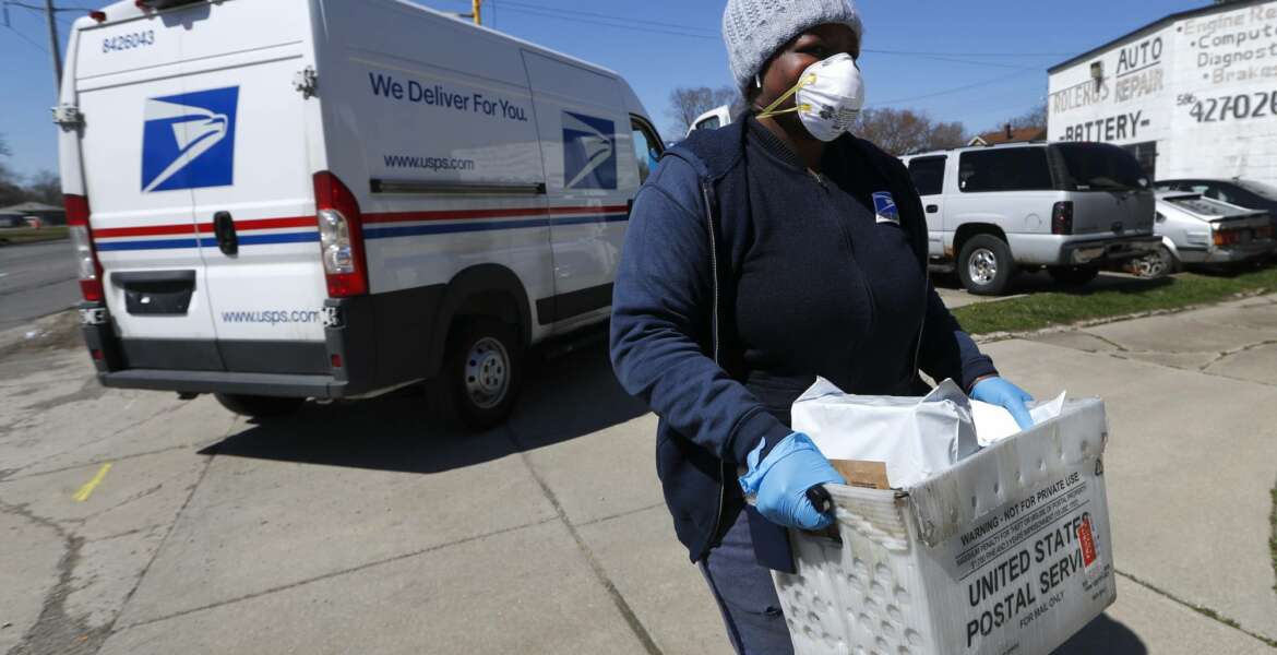 FILE - In this April 2, 2020 file photo, a United States Postal  Service worker makes a delivery with gloves and a mask in Warren, Mich. A group of states suing over service cuts at the U.S. Postal Service is asking a federal judge to immediately undo some of them, saying the integrity of the upcoming election is at stake.(AP Photo/Paul Sancya,File)