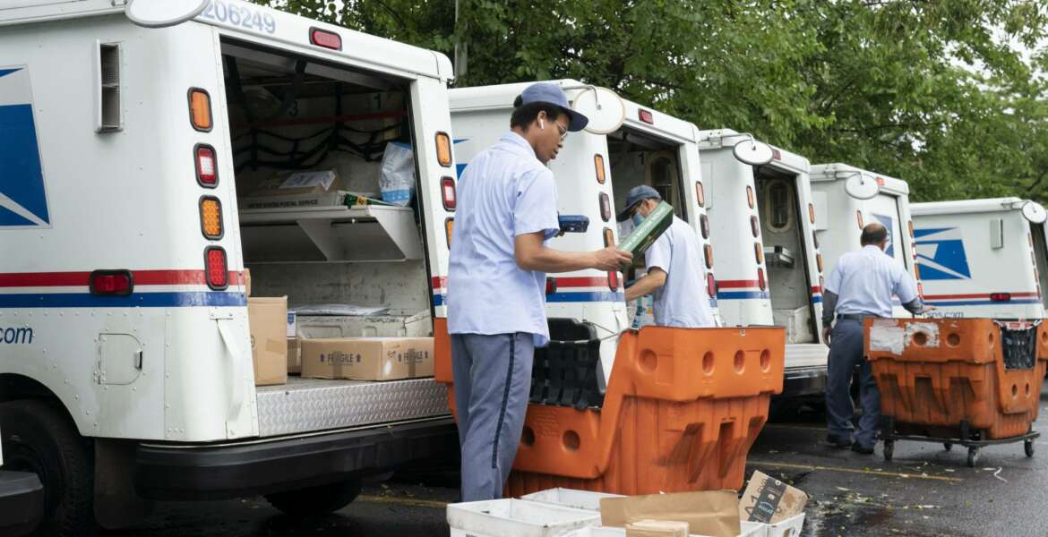 FILE - In this July 31, 2020, file photo, letter carriers load mail trucks for deliveries at a U.S. Postal Service facility in McLean, Va. A U.S. judge on Thursday, Sept. 17, 2020, blocked controversial Postal Service changes that have slowed mail nationwide. The judge called them 