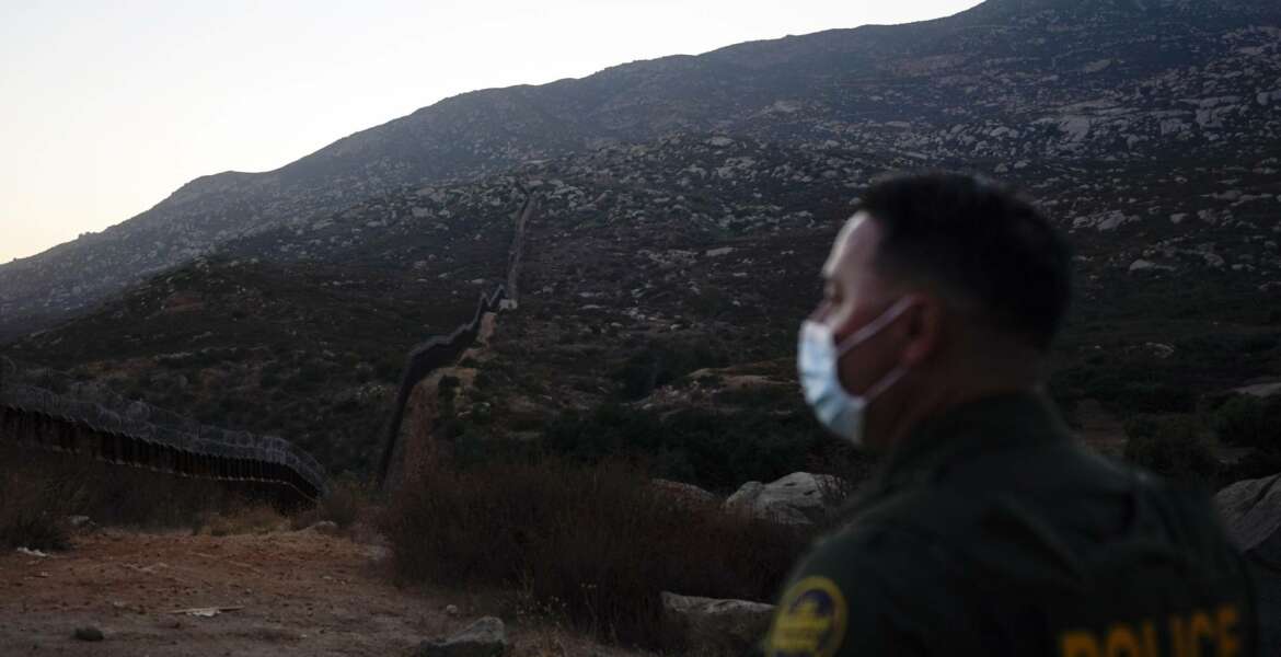 Border Patrol agent Justin Castrejon looks toward where the border wall makes its way over a mountain Thursday, Sept. 24, 2020, near Tecate, Calif. President Donald Trump’s reshaping of U.S. immigration policy may be most felt in his undoing of asylum. Castrejon says migrants pay $8,000 to $10,000 to be guided through the mountains and picked up by a driver once they reach a road. (AP Photo/Gregory Bull)