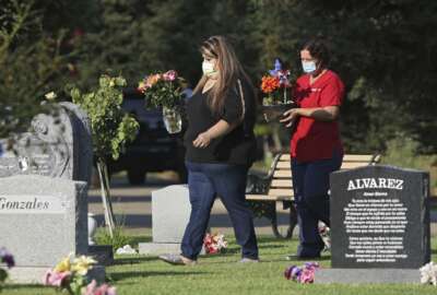 Lori Gonzalez, left, and Rachel Spray carry flowers to the temporary grave marker of Gonzalez's sister and Kaiser Permanente Fresno Medical Center nurse, Sandra Oldfield, at the Sanger Cemetery in Sanger, Calif., Saturday, Aug. 29, 2020. Oldfield died after being exposed to the novel coronavirus. Workers at the hospital said they did not have the proper personal protective equipment. (AP Photo/Gary Kazanjian)